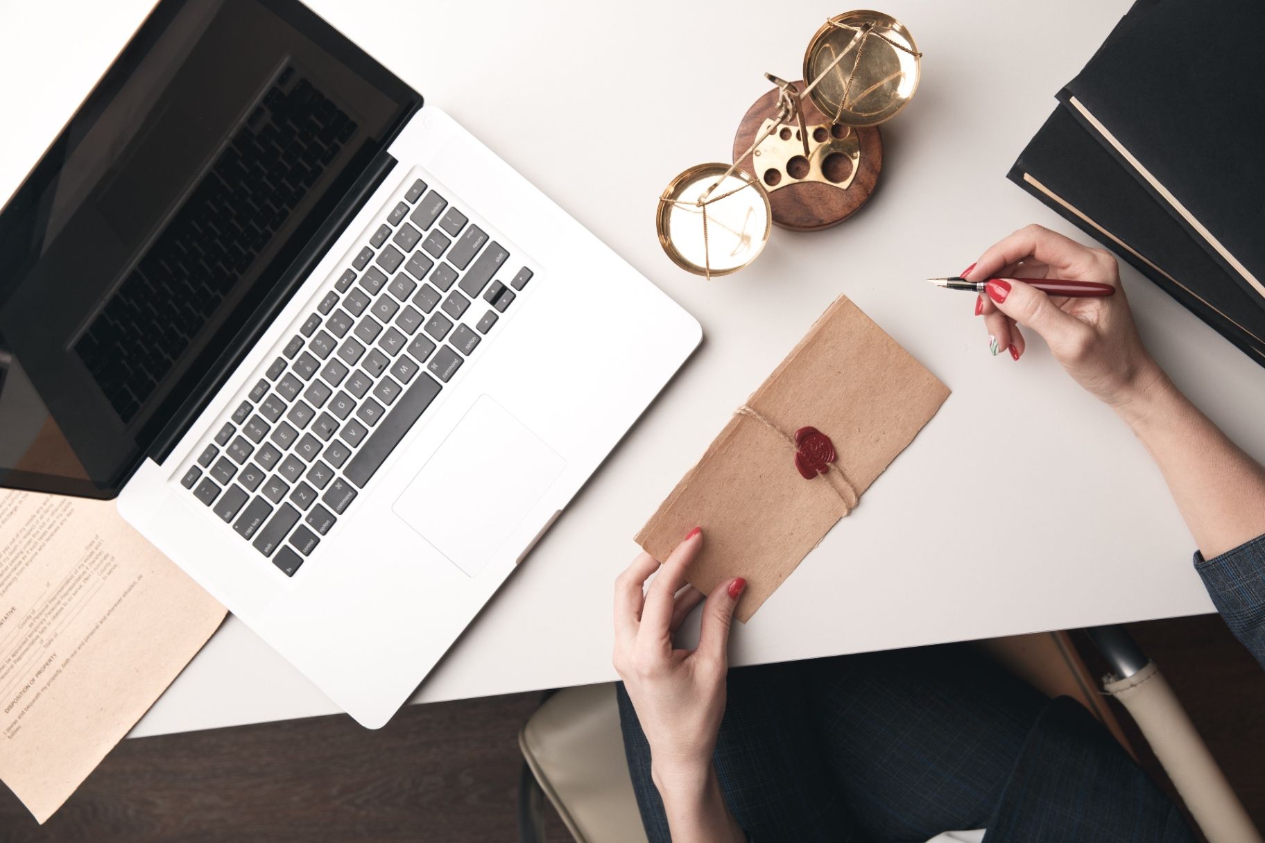 Overhead view of a desk with a laptop, legal document, brass balance scale, and kraft-paper envelope